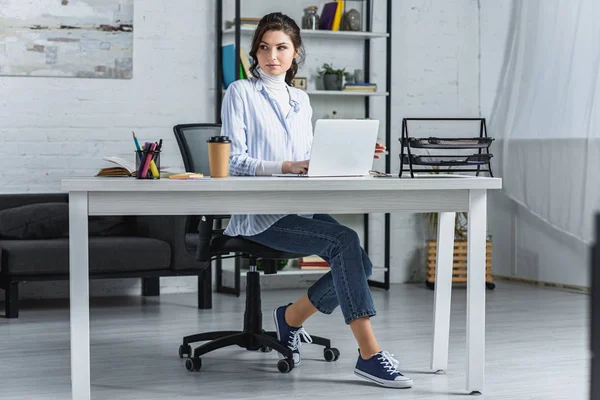 Femme attrayante utilisant sur ordinateur portable tout en étant assis dans le bureau moderne — Photo de stock