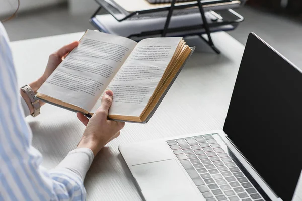 Vista ritagliata di donna che studia con libro vicino a computer portatile — Foto stock