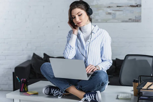 Attractive woman in headphones sitting on table with laptop — Stock Photo