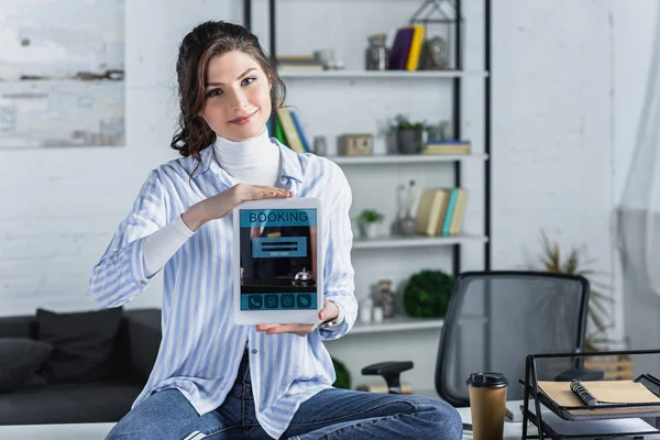 Mujer alegre sosteniendo tableta digital con aplicación de reserva en pantalla en la oficina moderna - foto de stock