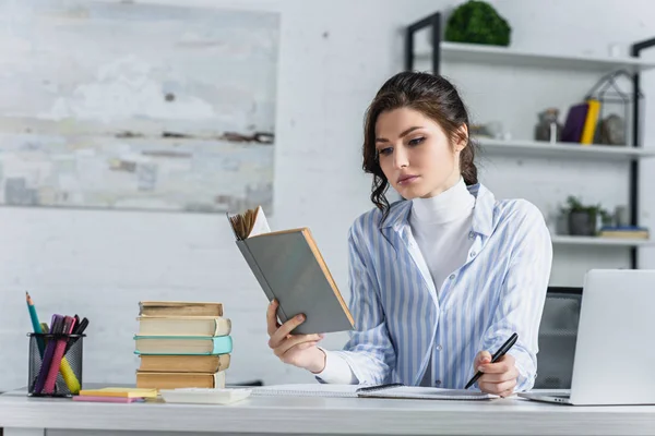 Mulher triste estudando com livro enquanto segurando caneta na mão no escritório moderno — Fotografia de Stock