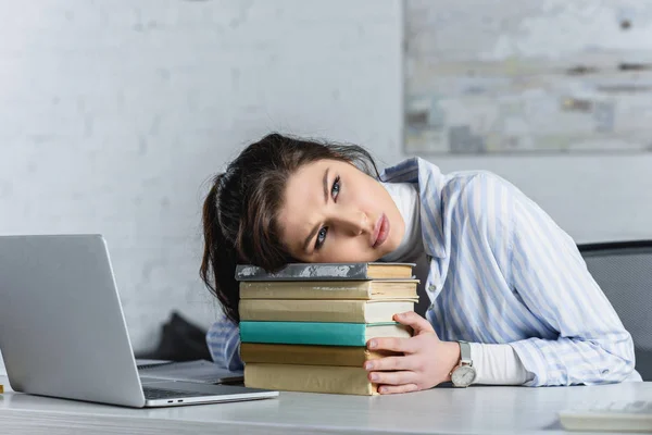 Tired woman lying on books near laptop in modern office — Stock Photo