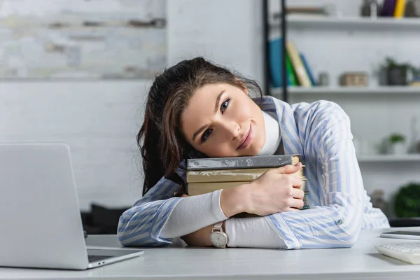 Mulher alegre que jaz em livros perto do computador portátil no escritório moderno — Fotografia de Stock