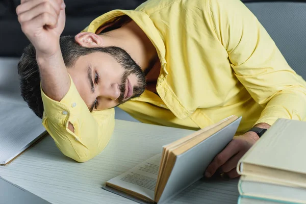 Tired man studying with book while lying on table in modern office — Stock Photo
