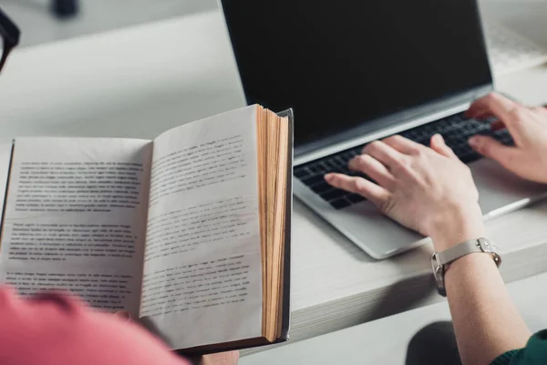 Fuoco selettivo di libro vicino a donna che scrive su computer portatile in ufficio moderno — Foto stock