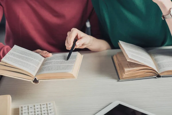 Cropped view of woman pointing at book with pen near coworker — Stock Photo
