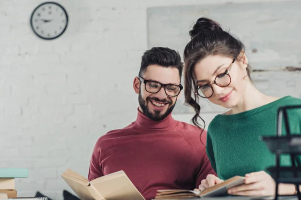 Schöner Mann mit Brille schaut attraktive Mitarbeiterin an, die mit Buch studiert — Stockfoto