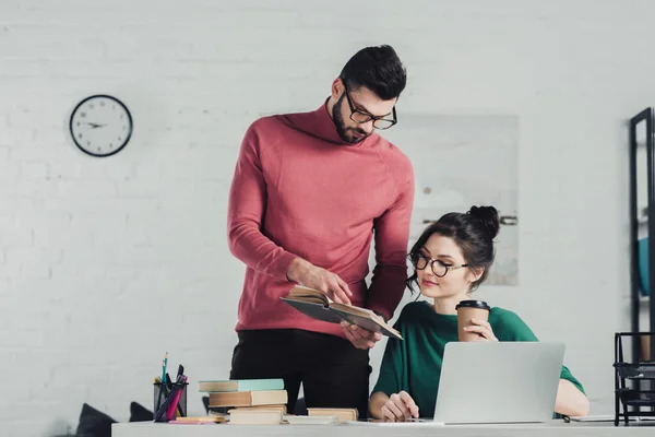 Handsome bearded man holding book near woman with paper cup — Stock Photo