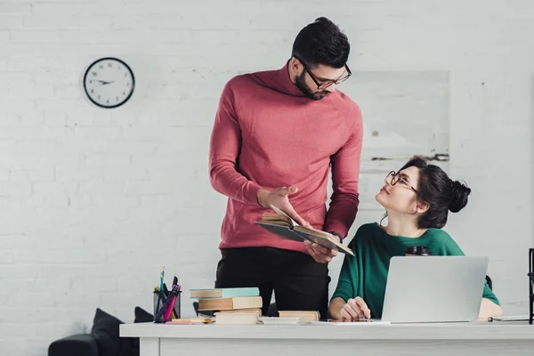 Handsome bearded man holding book near woman in glasses — Stock Photo