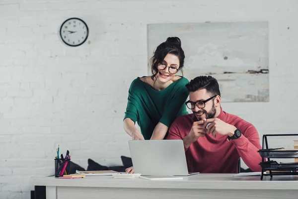 Attraktive Frau mit Brille blickt auf Laptop neben Mann in modernem Büro — Stockfoto