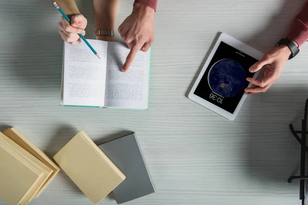 Top view of man pointing with finger at book near digital tablet with lock screen — Stock Photo