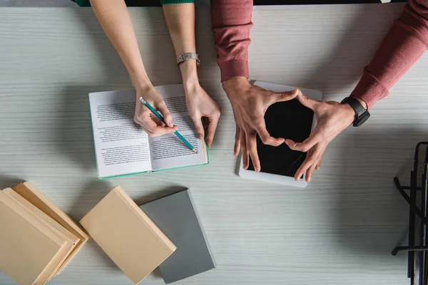 Vista dall'alto della donna che punta al libro con matita vicino all'uomo che fa cuore con le mani vicino al tablet digitale con schermo bianco — Foto stock