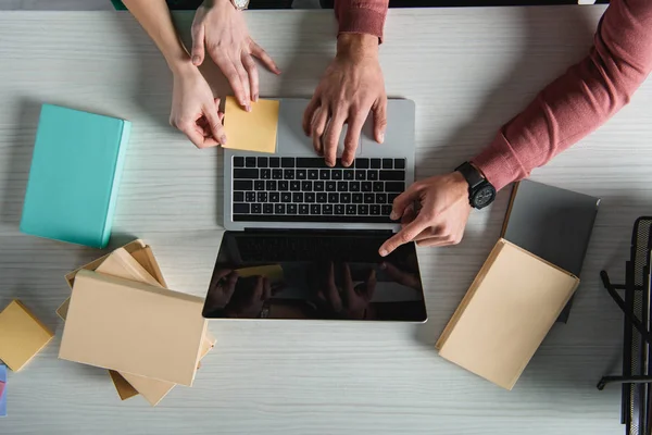 Vista superior do homem apontando com o dedo para o laptop com tela em branco perto da mulher segurando adesivo — Fotografia de Stock