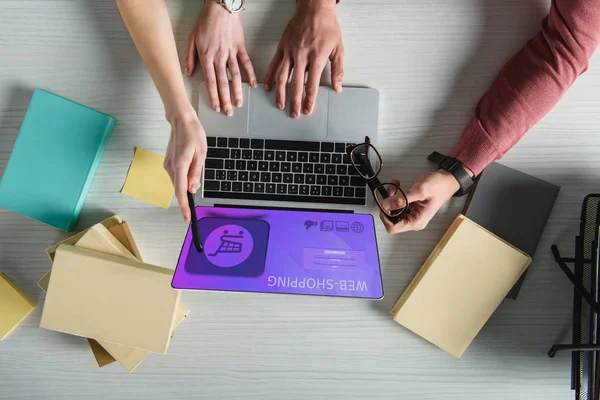 Vista recortada de la mujer apuntando a la computadora portátil con el sitio web de compras en la pantalla cerca del hombre sosteniendo gafas - foto de stock