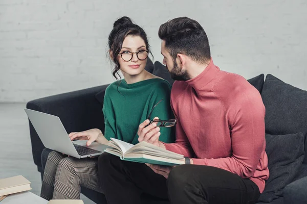 Homme regardant femme gaie dans des lunettes assis avec ordinateur portable — Photo de stock