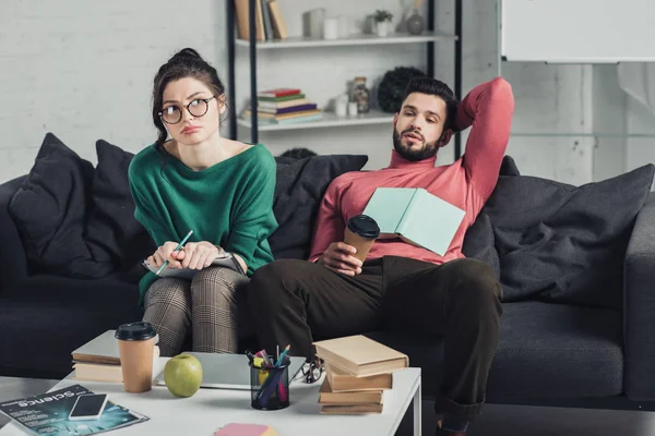 Bored woman in glasses holding notebook and pencil while sitting near handsome man — Stock Photo