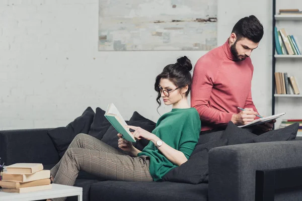 Attraktive Frau studiert mit Buch neben bärtigem Mann mit Notizbuch und Bleistift in der Hand — Stockfoto