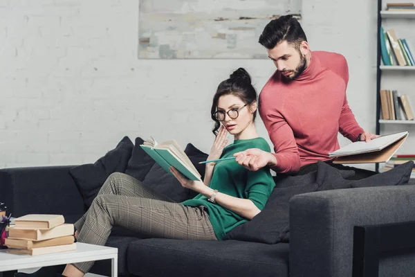 Uomo barbuto che punta al libro con la matita vicino donna sorpresa — Foto stock