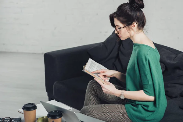 Attraktive Frau, die mit Buch studiert und auf dem Sofa sitzt — Stockfoto