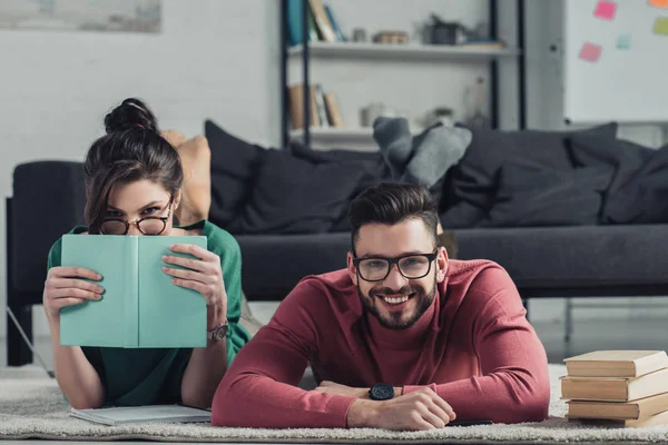 Fröhliches Paar in Brille auf Teppich neben Büchern liegend — Stockfoto