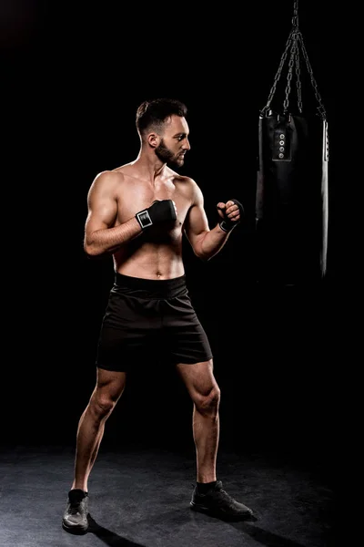 Handsome boxer kicking boxer bag on black background — Stock Photo