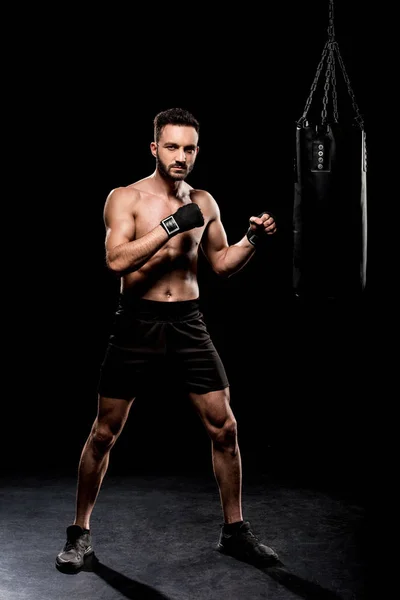 Schöner Boxer, der in die Kamera neben der Boxertasche auf schwarzem Hintergrund blickt — Stockfoto