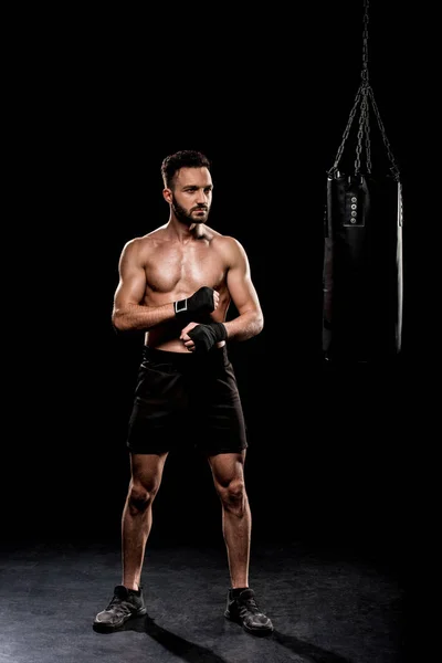 Boxeador sin cortocircuito muscular de pie cerca del saco de boxeo sobre fondo negro - foto de stock