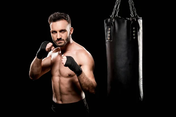 Muscular boxer kicking punching bag isolated on black — Stock Photo