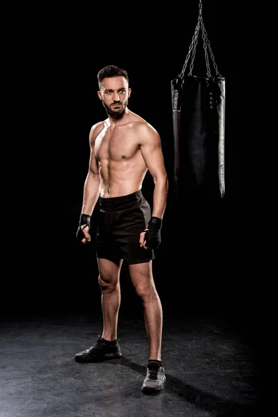 Pugile muscoloso guardando sacco da boxe su sfondo nero — Foto stock