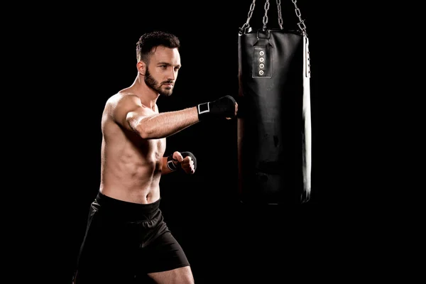 Boxeador muscular golpeando saco de boxeo aislado en negro - foto de stock