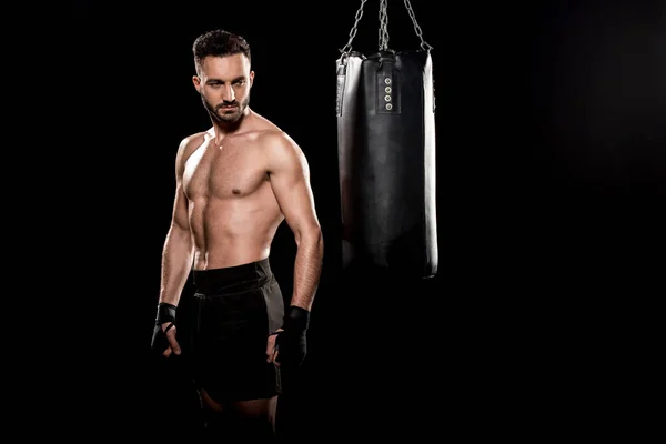 Boxeador sin cortocircuito muscular mirando saco de boxeo aislado en negro - foto de stock