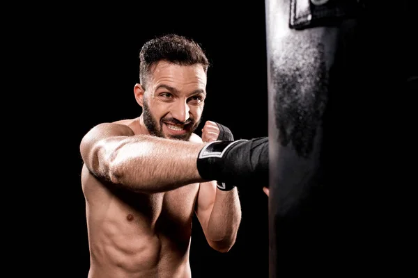 Guapo sin cortocircuito deportista golpeando saco de boxeo aislado en negro - foto de stock