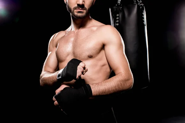 Cropped view of shortless athlete wrapping up gloves on black background — Stock Photo