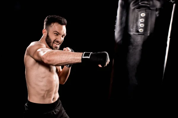 Apuesto deportista patadas bolsa de boxeo aislado en negro - foto de stock