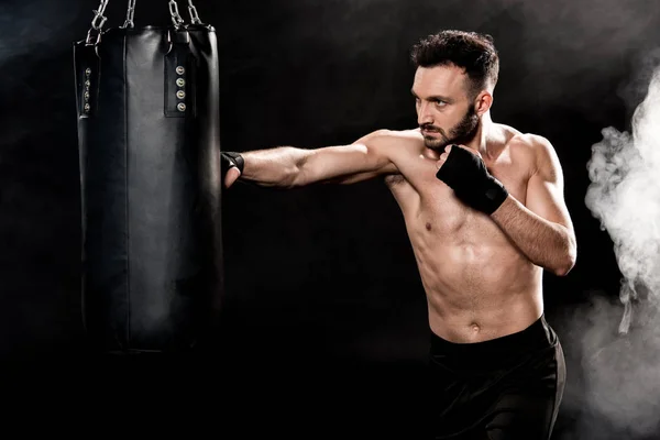 Bonito atlético boxer bater perfurando saco no preto com fumaça — Fotografia de Stock