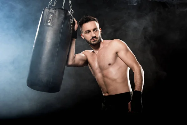 Thoghtful boxeador atlético que sostiene el saco de boxeo en negro con humo - foto de stock