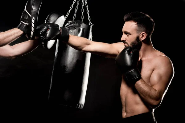 Boxeador muscular luchando con el hombre en guantes de perforación aislados en negro - foto de stock