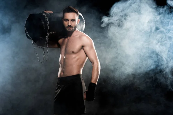 Boxeador muscular que sostiene el saco de boxeo en el hombro negro con humo - foto de stock