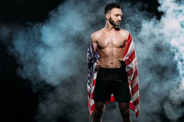 Atleta muscular sosteniendo bandera americana sobre negro con humo - foto de stock