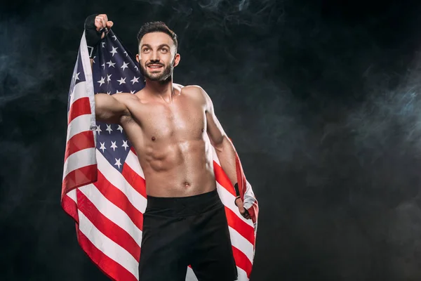 Happy athlete holding american flag on black with smoke — Stock Photo