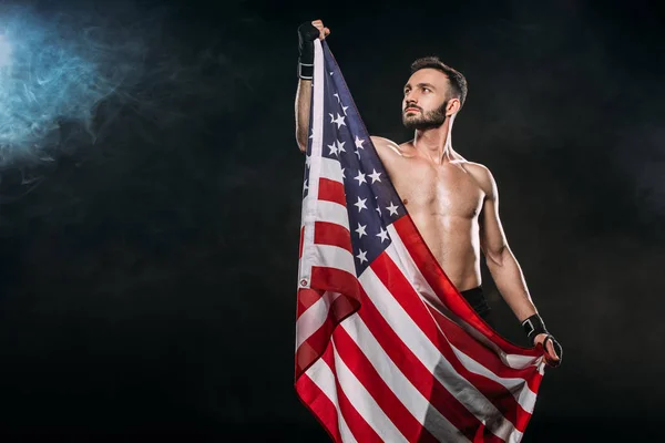 Beau sportif tenant drapeau américain sur noir avec de la fumée — Photo de stock