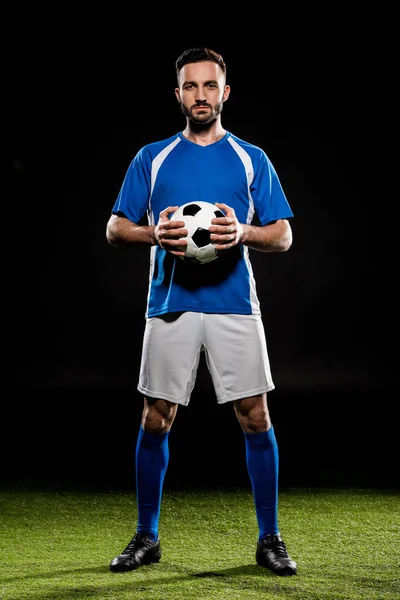 Giocatore di calcio in piedi con palla su erba verde isolato su nero — Foto stock