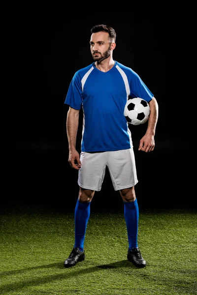 Forte giocatore di calcio in piedi con palla su erba verde isolato su nero — Foto stock