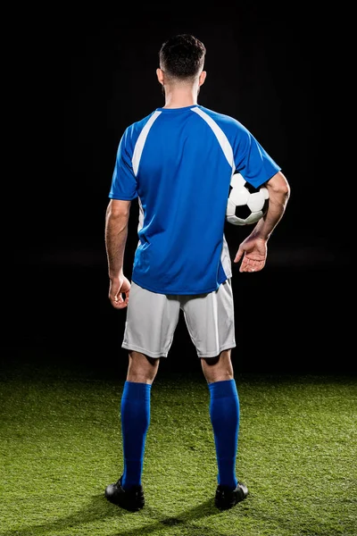 Back view of sportsman holding ball and standing on grass isolated on black — Stock Photo