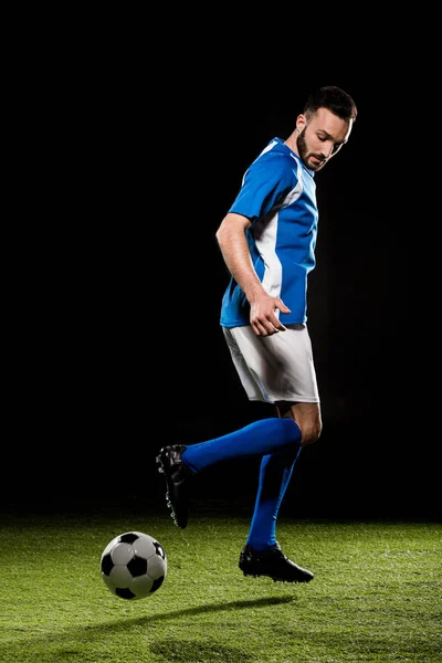 Muscular sportsman in uniform playing with ball isolated on black — Stock Photo