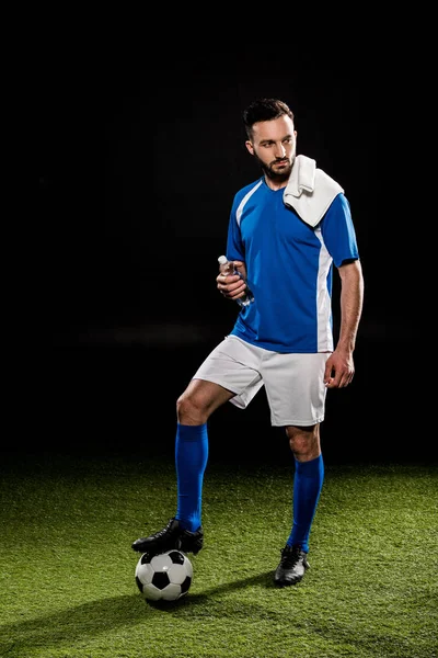 Hombre guapo en uniforme de pie con toalla en el hombro y la celebración de botella aislada en negro - foto de stock