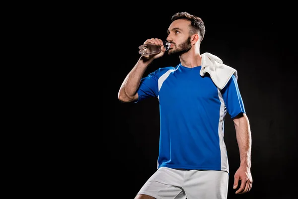 Bearded man in uniform standing with towel on shoulder and drinking water from bottle isolated on black — Stock Photo