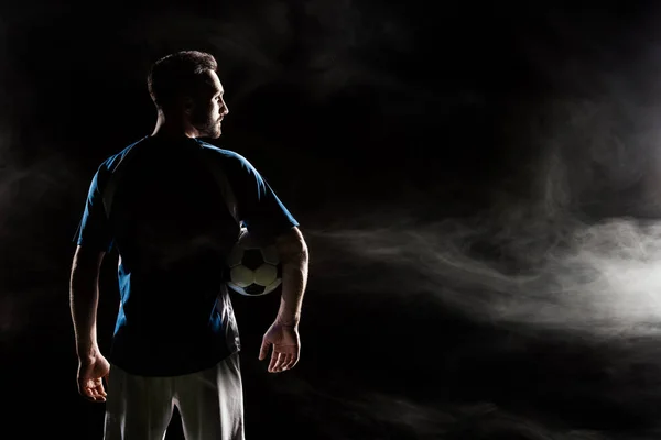 Silhouette of football player holding ball on black with smoke — Stock Photo