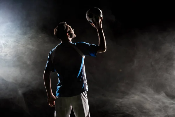 Silhouette of player in uniform holding ball above head on black with smoke — Stock Photo