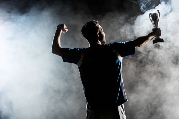Silhouette of man standing with trophy on black with smoke — Stock Photo